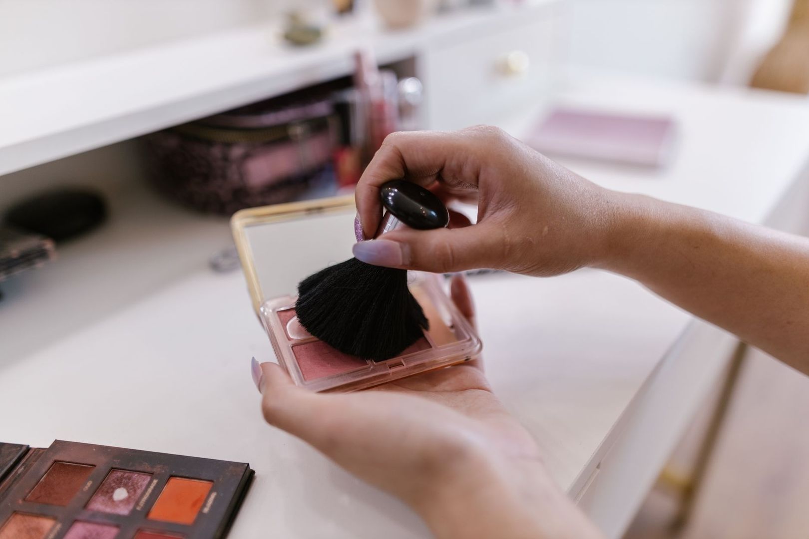 Sminkborste sveper över en palett med rosa rouge vid makeupbordet